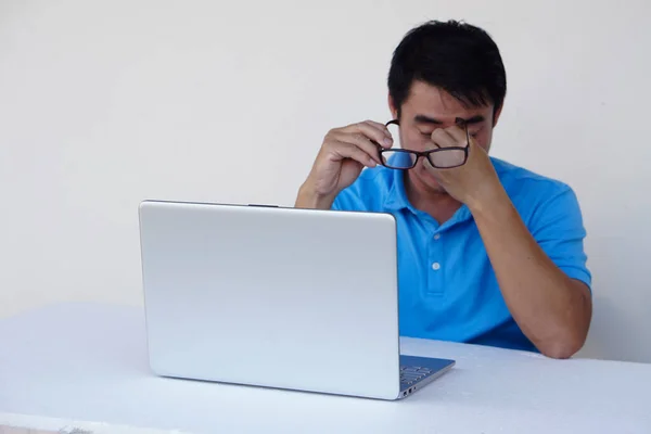 Asian man, feels hurt his eyes, holds eyeglasses during working on laptop. concept : Eyesight problem. Optometry. Glasses with convex or concave lenses. Myopia.Eye disease