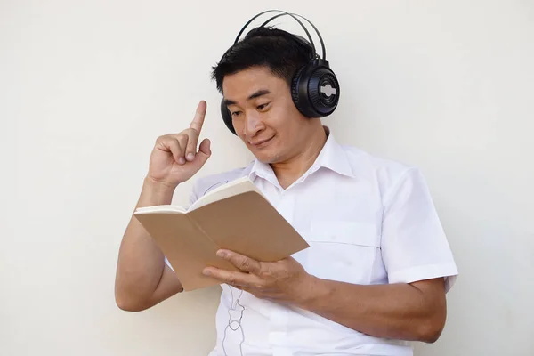 Asian man reads book and wears headphone listen to soft music to make concentration in reading. Get idea. Concept, free time, pastime, hobby, Relax with music.