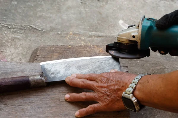 Closeup hands are sharpening a knife with electric sharpener grinder machine in motion action of sparking. Concept, traditional style of fixing tool.