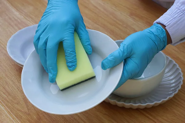 Hands use sponge scrubber to clean dish. Concept, daily chore, household cleaning kitchen utensils. Wear protective gloves to protect hands from chemical substances allergy.