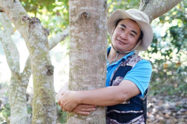 Handsome Asian man botanist hugs trunk of tree in forest. Concept, Love nature and protecting, Forest ,ecology and environment conservation. .         