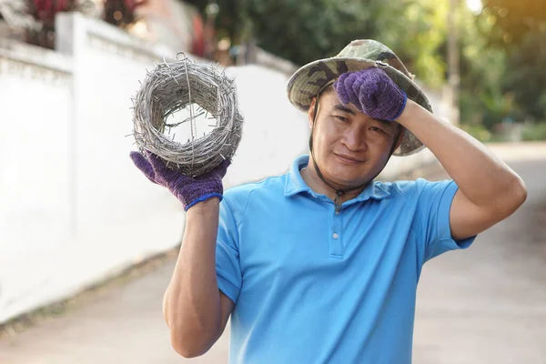 Asian man worker holds roll of barbed wire, feels tired. Concept, construction tool. Barbed wire is used for make fences , secure property ,make border to show the territory of  area.