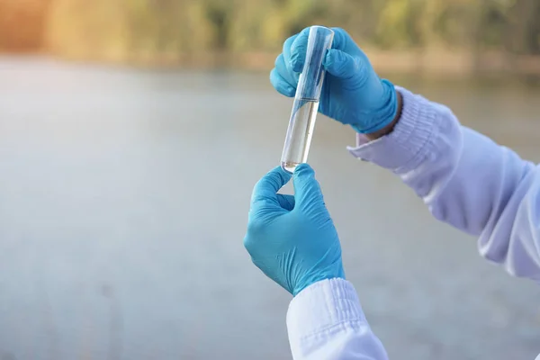 Closeup researcher hands wears blue gloves holds test glass tube that contain sample water from the lake. Concept, explore, inspect quality of water from natural source.