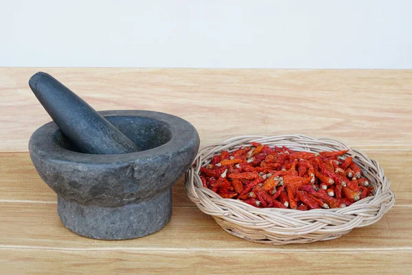 Old granite stone mortar with pestle and basket of red dried chillies for cooking.