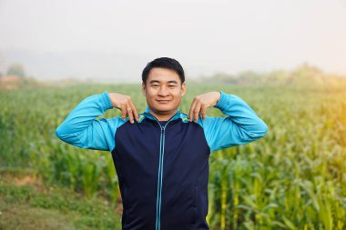Handsome Asian man workouts  outdoor. Put hands on shoulders. Warm up before or cool down after exercise. Concept, health care. Sport  creative activity. Give time for yourself.       