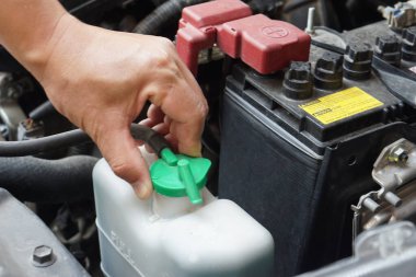 Tamircinin eli otomobilin soğutucu seviyesini kontrol etmek için araba motorunda bir şişe su açıyor. Konsept: Kontrol ve bakım servisi.       