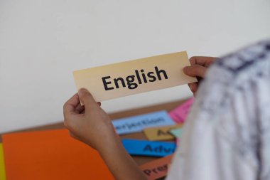 Closeup student's hands  hold English word card. Concept, education, learning and studying language. Education. Reading and memorizing strategy of learning process for kid. Practice makes perfect.    clipart