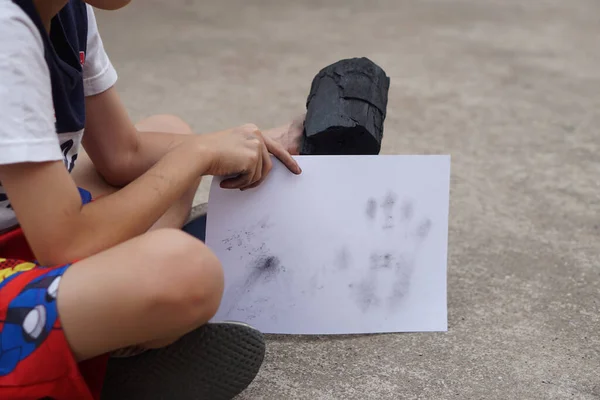 Close Up boy holds white paper with stain of black charcoal, make hand print graffiti. Concept, learning by doing. Touch and observe  in science subject activity. Nature fuel
