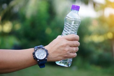 Yakın çekim elinde mor kapaklı su şişesi var. Kavram: Sağlık için içme suyu, sağlıklı yaşam tarzı. Susuzluğu giderir, yorgunluğu azaltır, vücudu tazeler.. 