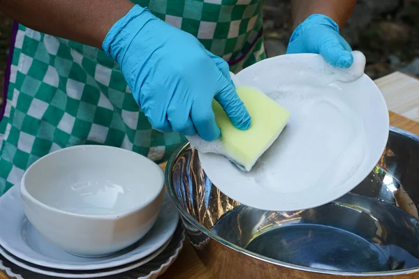 Closeup hand wears blue gloves, holds sponge to wash dish. Concept daily chore, housework. Cleaning after meals. Duty in kitchen.