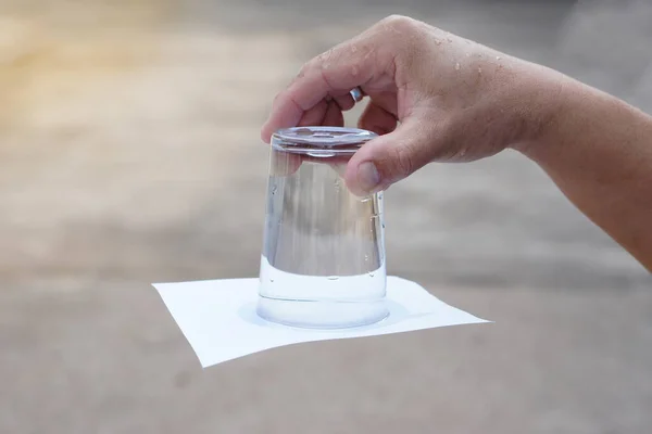 闭合的手握住并把一杯水翻下来 玻璃杯盖满了纸 空气和液体压力的概念 科学实验 轻松的科学科目活动 — 图库照片