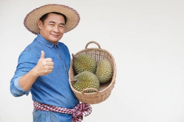 Yakışıklı Asyalı çiftçi şapka takıyor, mavi gömlek giyiyor, elinde durian meyveleri sepeti var, başparmaklar havada. Kavram, tarım işgali. Taylandlı çiftçiler ekonomik ve ihracat meyveleri olarak durian meyveleri yetiştiriyor    