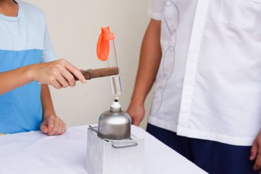 Kapanış öğrencisi balondaki havanın reaksiyonuyla ilgili bilimsel deney yapıyor. Test tüpündeki su kaynıyor. Kavram, bilim kampı aktivitesi. Yaparak öğreniyorum..   
