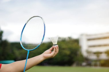 Kapalı el badminton raketi ve açık havada servis horozu tutuyor. Konsept, spor ekipmanları, spor yapmak ve sağlık için egzersiz yapmak, eğlence aktivitesi.                