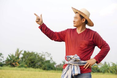 Asyalı çiftçi şapka takar, kırmızı gömlek giyer, elini beline koyar, parmağını kaldırır. Kendinden emin. Kavram, tarım işgali. Taylandlı çiftçi. Metin veya reklam eklemek için boşluk kopyala.  