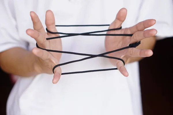 Closeup boy hands is playing rope which called cats cradle game. Concept, game involving the creation of various style figures between the fingers. Traditonal playing.
