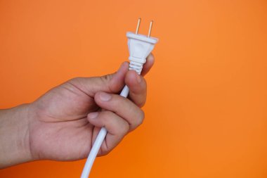 Elektirik kablosu tutan erkek eli yakın plan, turuncu arka plan. Kavram, elektrik gücünden tasarruf etmek. Elektrikli aletleri kullandıktan sonra her seferinde kapatma kampanyası.  