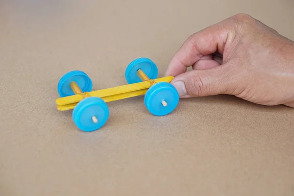 Hand hold handmade toy racing car made from ice cream sticks and bottle caps. Concept, Recycling kids toy. Easy to do, creative DIY craft that kids can do. Fun lesson