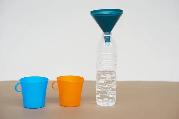 青とオレンジのカップ 水と上の漏斗のボトル 実験装置 液体量の測定 — ストック写真