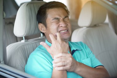 Asyalı bir adam arabada incinmiş bir şekilde oturuyor. Kavram, bilek ağrısı, uzun yoldan gelen kramplar. Sağlık sorunları. Kazaya neden olabilecek sağlık sorunları olan bir hasta için uygun değil..        