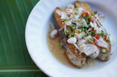 Kızarmış Kral uskumru salatası, beyaz tabakta. Kavram: aşçılık. Deniz ürünleri. Taylandlıların pirinçle yediği lezzetli menü ve tuzlu balıklı menü. Tayland mutfağı. Muz yaprağı arkaplanı