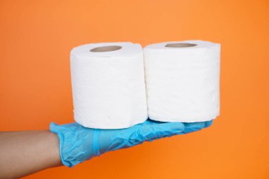 Turuncu arka planda izole edilmiş beyaz kağıt rulo el ele tutuşun. Kavram, temizlik aleti, kirliliği temizlemek ve ıslaklığı emmek için hijyenik, hijyenik ve hijyenik tuvalet kağıdı kullan.  