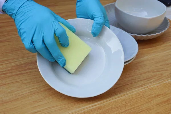 Closeup hand wear blue gloves, hold sponge to wash dish. Concept daily chore, housework. Cleaning after meals. Duty in kitchen. Wear protective gloves to protect hands from chemical substances allergy