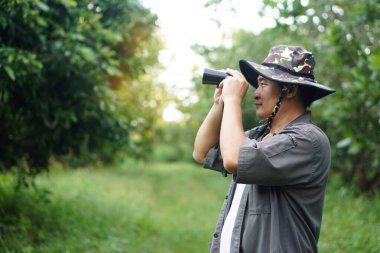 Asyalı ekolojist ormandaki doğayı incelemek için dürbün kullanır. Kavram, doğa keşfi. Ekoloji dersi. Hobi aktivitesi, yaşam tarzı. Çevreyi keşfet. Yalnız seyahat etmek.         