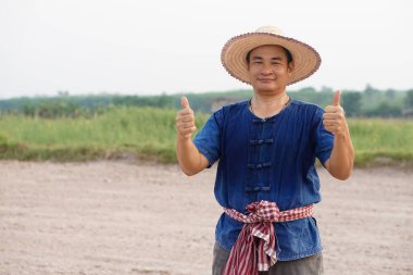 Yakışıklı Asyalı çiftçi Taylandlı geleneksel kostüm, şapka, mavi gömlek giyer, başparmak yukarı, kendinden emin hisset. Kavram, Tarım İşgali.    