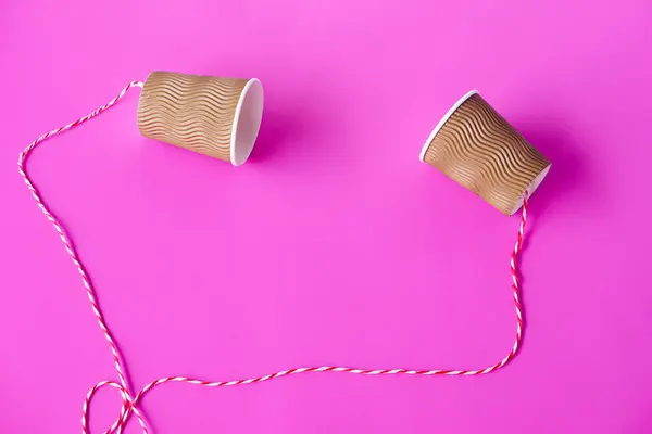 DIY paper cups with string on pink background. Concept, telephone toys which apply with science knowledge about vibration sound through straining strings causing us to hear the sound.
