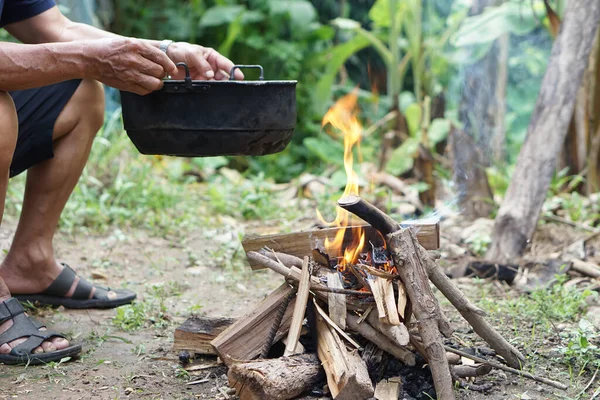 Close up man holds old black pot to cook on bonfire. Concept, cooking outdoor, kitchen in forest. Survival life skill for camping or hiking. Rural traditional lifestyle. Lighting fire with wood.