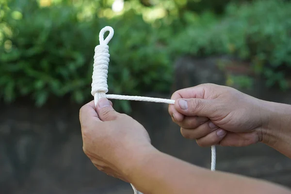 Close up hands tying white rope, Keeping long rope to be shorter. outdoor background. Concept, practice to tie different pattern of rope to apply in daily life such as tying things or doing  activity.