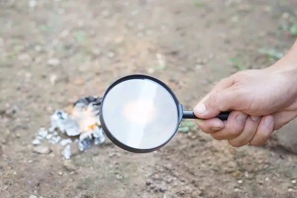 Close up hand hold magnifying glass to make fire for burning paper. Concept, Scicence experiment about convex lens, hold magnifying glass between the sun and tinder. Handy survival skill