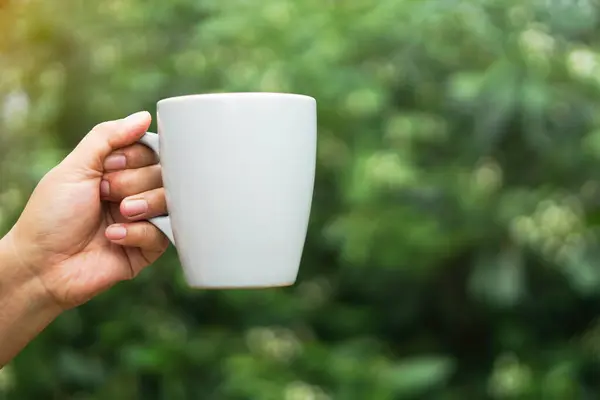 Close up hand hold ceramic mug, outdoor nature background. Concept, relax time with favorite beverage.Take a break with coffee, hot chocolate or tea. Reusable and washable cup. Eco friendly lifestyle.