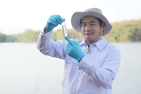 Asian man environment researcher holds tube of sample water to inspect from the lake. Concept, explore, analysis water quality from natural source. Ecology field research.