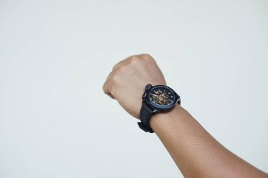 Kapalı kapılar ardında siyah bir saat takıyor. Kavram, zaman anlatmak için modaya uygun aksesuar, şık, dakik ve zeki görünmeni sağlar. Analog kol saati.