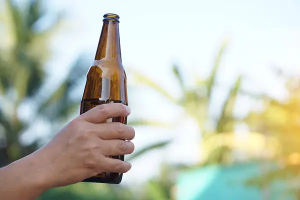 Hand holds bottle of beer, outdoor background. Concept, relax time with soft alcoholic beverage after work, day off, holiday , vacation or party. Celebration.