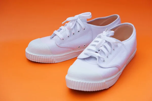 Pair of new white canvas sneakers,  Orange background. Comfortable, fashionable style. Concept, shoes for doing sport or exercise also can wear for traveling, hiking or doing active activity.