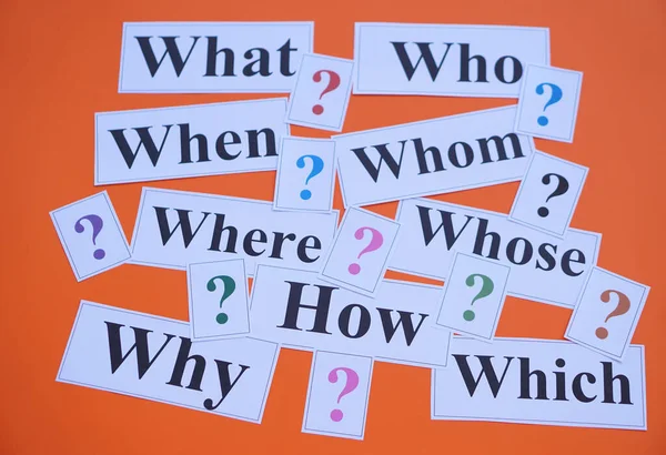 Paper cards with Wh-question words and question marks on orange background. Concept. Teaching aid. Education materials for teach WH- question. Asking questions. Suspicious symbol to find answer.