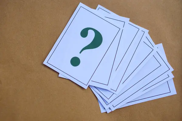 Overlapped pile of paper cards of green question mark on brown background. Concept. Teaching aid. Education materials for doing activity or playing games about find answers.