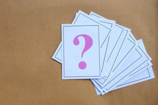 Overlapped pile of paper cards of pink question mark on brown background. Concept. Teaching aid. Education materials for doing activity or playing games about find answers.