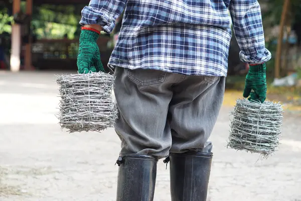 Back view of man worker is carrying rolls of metal barbed wire. Concept, construction tool. Barbed wire is used for make fences , secure property ,make border to show the territory of area.