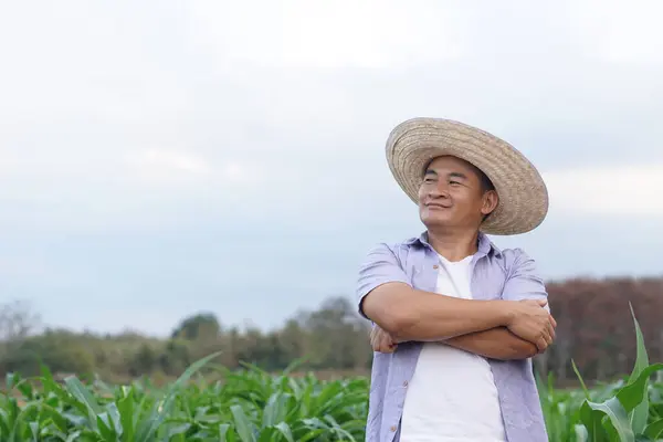 Handsome Asian man farmer is at garden, wears hat, cross arms on chest, feels confident. Concept, Agriculture occupation. Thai farmer lifestyle, Feeling proud and satisfied in crop production