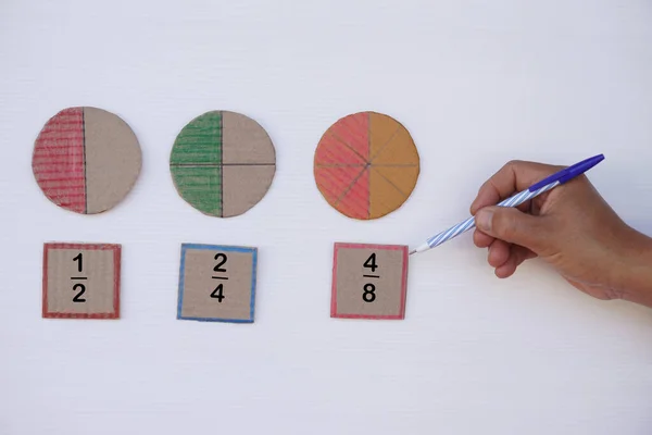 Math teaching materials about fraction. Hand hold pen to point at circle paper to show parts of color separation. Concept, education. DIY craft as teaching aid in Math subject.