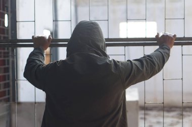 Kapüşonlu bir adamın geçmişe bakışı, metal bir hapishanede alıkonuldu. Kavram, suç. Cezalandırma. Gözaltı. Suçlular. Özgürüm. Özgürlüğü bekliyorum..   