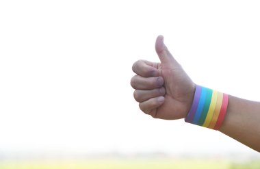 Eller gökkuşağı renginde çizgili bileklik takar, başparmaklar yukarı. Konsept, Lgbtq + onur ayında, Haziran. Dünya çapındaki LGBT topluluğunun sembolü. İnsan cinsiyet çeşitliliğinin desteklenmesi.           
