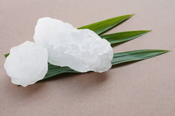 White crystal alum stones or Potassium alum on green leaves. Chemical compound. Useful for beauty and spa treatment. Use to treat body odor under the armpits as deodorant and make water clear.