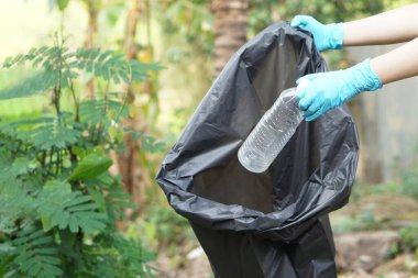 Kapalı eller siyah çöp torbasına koymak için plastik şişeyi tutar. Konsept, çöp yönetimi, yeniden kullanılmış, geri dönüştürülmüş plastik şişeler. En iyi çevre için temiz ve kamu hizmeti yapın. Sıfır atık. 