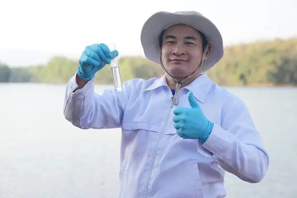 Asian man environment researcher holds tube of sample water to inspect from the lake. Concept, explore, analysis water quality from natural source. Ecology field research.