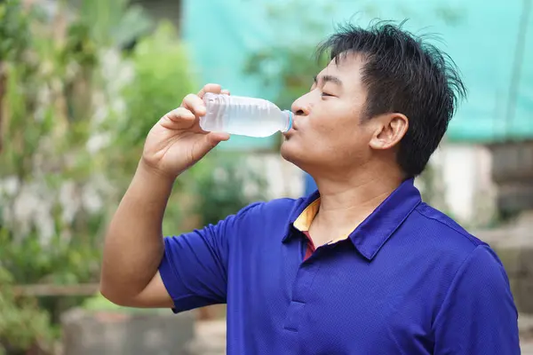 Asian man is drinking cool water from bottle. Concept, Drink water for good health. Relief from thirsty, and protect from heat stroke, cool down in hot weather condition. Health care.